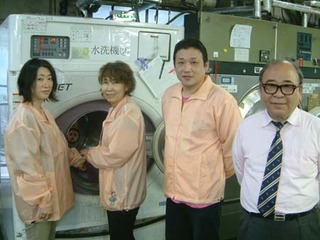大型洗濯機の前に並ぶ団体メンバーの写真